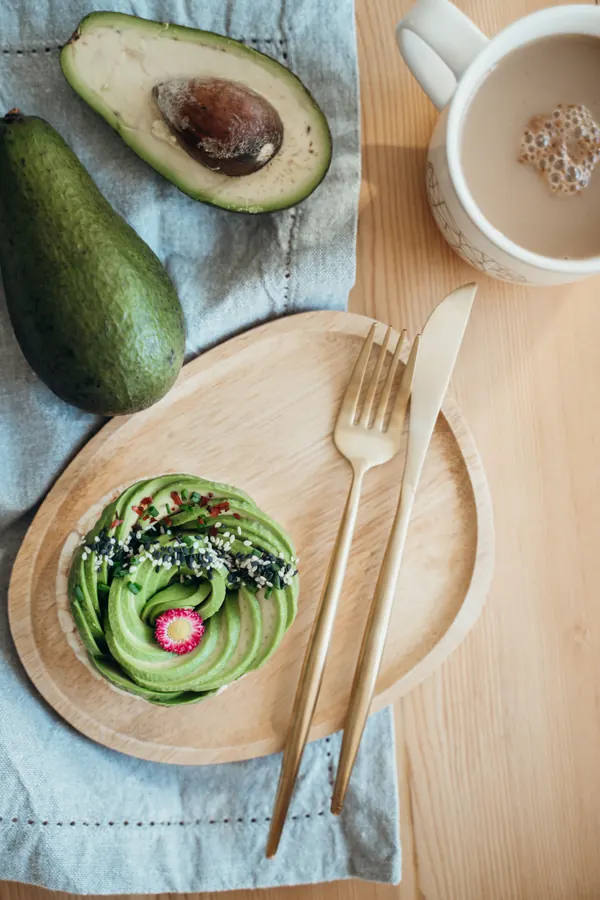 Tostada de palta en plato de madera junto a un café